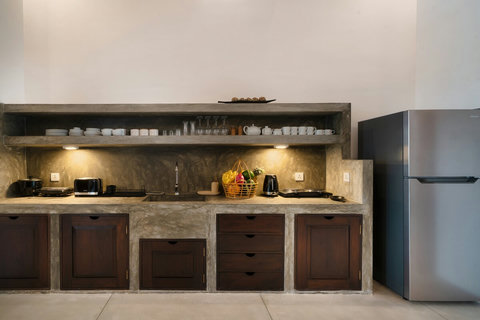 Close-Up of Kitchenette- A fully equipped concrete-finish kitchenette with all essentials—cookware, dishes, fridge, and a fresh fruit basket ready for your stay.
