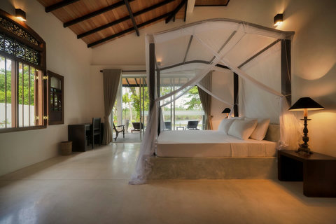 A serene, spacious river-view bedroom with a luxe canopy bed- High timber ceilings, soft lighting, and elegant furnishings, opening onto a private veranda with peaceful views of the garden and river. Perfect for a calm and comfortable stay.