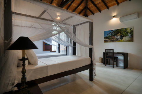 A spacious bedroom with two elegant canopy beds.- Perfect for families, this bright room features high wooden ceilings, airy mosquito nets, and plenty of space. A baby cot can be added upon request for your convenience.
