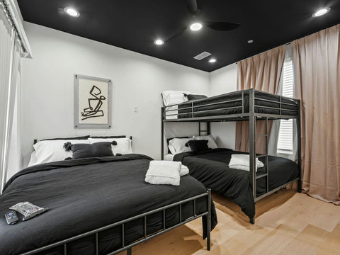 This stylish black-and-white bedroom features one queen bed and a queen bunk bed next to the rooftop, perfect for families or group. The modern decor creates a sleek, inviting space that is both comfortable and functional for a restful stay. 
