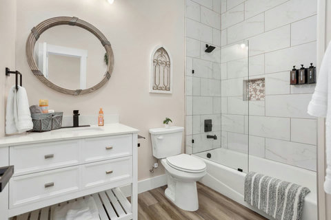 Bright spa-style bath with marble tile, glass panel and black fixtures.
