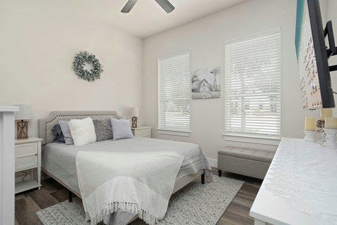 Bright, serene bedroom with queen bed, ceiling fan, bench & smart TV.