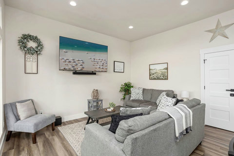 The open living area features a cozy sofa and a love seat. Large windows allow natural light to fill the room, providing stunning views of lush greenery and a running river. The space is tastefully adorned with soft cushions and decorative accents.