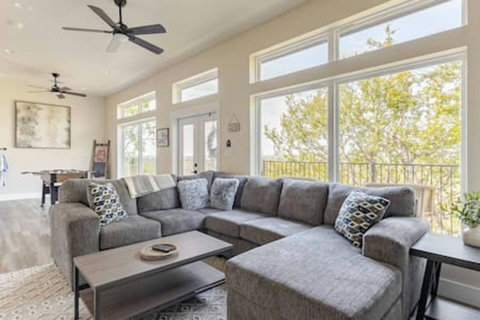 The spacious living area includes a cozy sectional sofa, an app-streaming TV, and a game room with a foosball table. High ceilings and large windows with an epic view invite guests to relax and have fun.