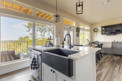 The kitchen boasts modern white cabinetry, countertops, and appliances, establishing a sleek contemporary vibe. A spacious island, topped with white quartz, offers ample preparation space, accompanied by seating for informal dining.