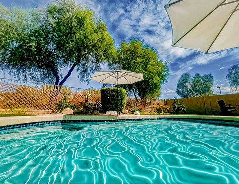 Sunny private pool with shaded umbrellas and a lush backyard setting