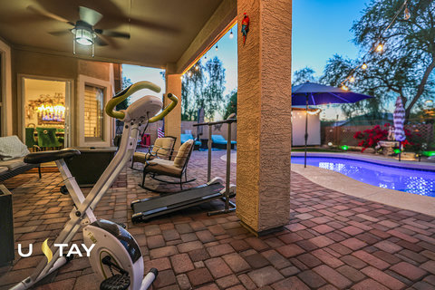 Covered patio gym and lounge space beside a glowing resort-style pool
