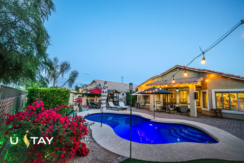 Resort-style backyard with glowing pool, patio seating, and string lights