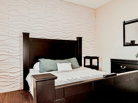Modern room with 3D accent wall, dark wood bed, cozy linens.