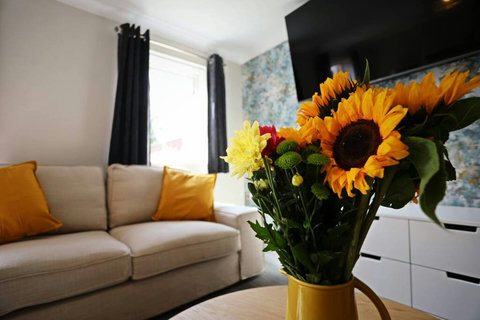 Living room featuring two-seater sofa, two armchairs, TV, storage space, table and chairs.