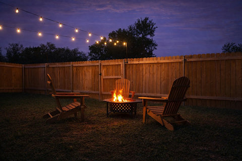 Fire pit glowing under string lights in the fenced backyard