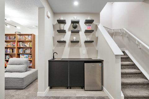 Fully equipped basement wet bar with elegant black cabinetry and curated display shelves