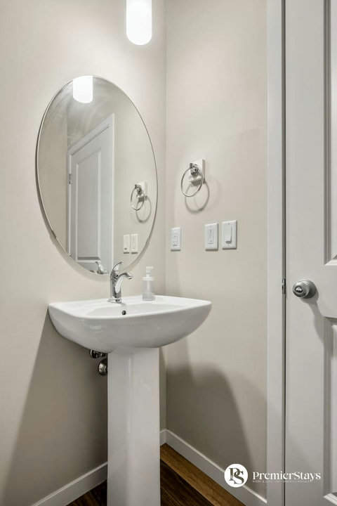 Bright, clean half bath featuring a pedestal sink and stylish round mirror
