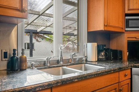 Bright kitchen with granite counters, double sink, and natural light from garden views