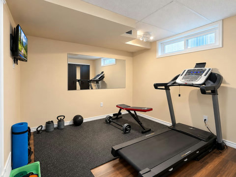 Basement gym with treadmill, exercise bench and weights. The portable queen mattress and its linens are stored in the gym closet.