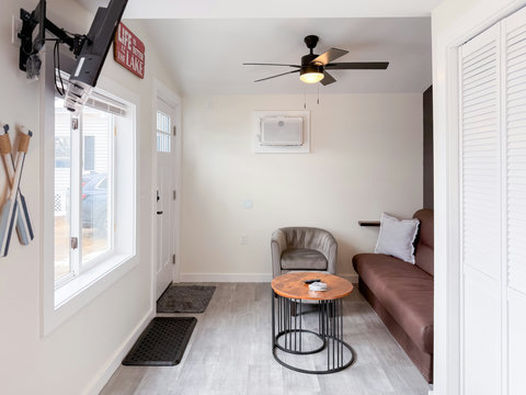 Bright, open lounge area with wall-mounted TV, ceiling fan, air conditioning, and view of the lake — everything you need, nothing you don't.