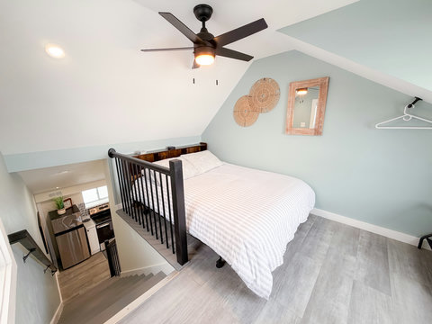 Cozy loft bedroom with vaulted ceilings, bedroom retreat with vaulted ceiling, queen bed, ceiling fan, ceiling-mounted smart TV, lake-view window, and luggage racks — everything you'd want after a day on the water.