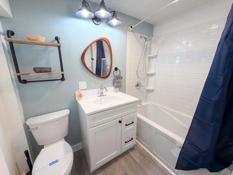 Freshly renovated full SPA bathtub with shower combo, artisan wood-framed mirror, industrial-chic shelving, and spa-blue accents — spotlessly clean for every stay.
