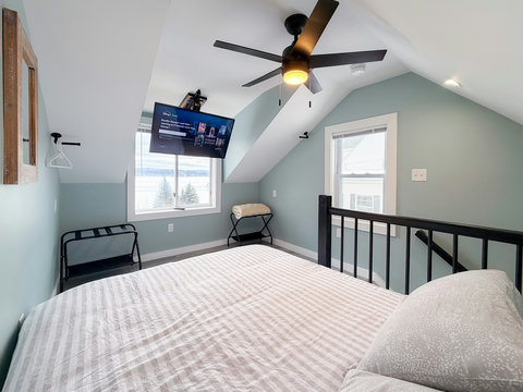 Cozy loft bedroom with vaulted ceilings, TV, and bright natural light
