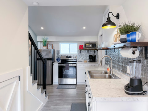 Open kitchen with full stainless appliances, vintage-style backsplash and dark wood and iron shelving, and easy stair access to the upper bedroom suite. Bright kitchen with stainless appliances.