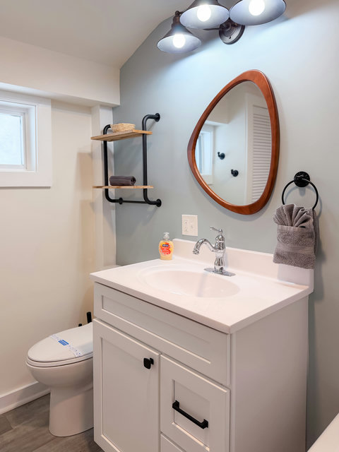 Bright modern bathroom with stylish vanity, custom mirror, and open shelving