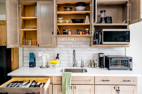 Decked out with convection oven/airfryer, coffee maker, blender, microwave, hot water kettle, dishes, utensils, knife set and cutting board, cooking spices, waffle maker, tupperware, bowls, colander and toaster. Cleaning supplies under sink.

