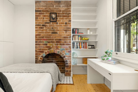 A peaceful bedroom with original brickwork, a decorative fireplace, built-in shelving and a practical desk.