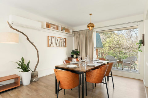 Gather around the dining table with leafy views and natural light creating a relaxed coastal atmosphere
