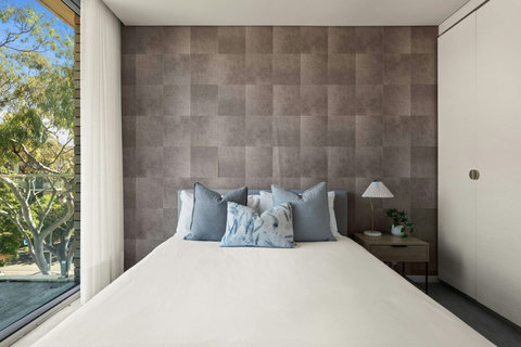 Queen bedroom with a textured feature wall, built-in storage and leafy views through the glass doors