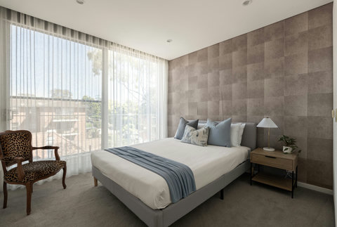 Queen bedroom with a textured feature wall, soft natural light and leafy views through the full-height windows