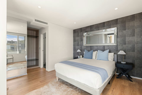 Spacious bedroom with a queen bed, built-in storage and a stylish feature wall behind the bed