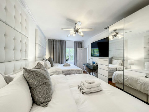 An elegantly spacious designer bedroom boasting two luxurious KING-size beds, a sleek professional workspace, and multiple mirrored closets that create a bright, open, and sophisticated atmosphere.