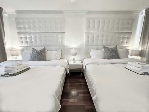 An elegantly spacious designer bedroom boasting two luxurious KING-size beds, a sleek professional workspace, and multiple mirrored closets that create a bright, open, and sophisticated atmosphere.
