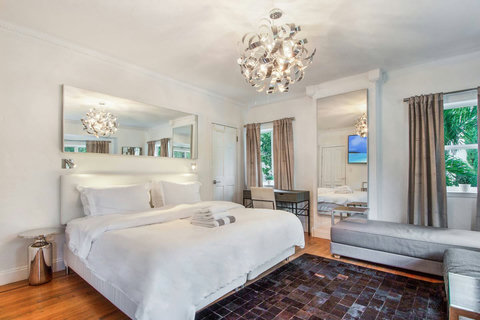 An elegantly designer bedroom boasting a luxurious KING-size beds (or 2 twin beds upon request), a sleek professional workspace, designer sofa daybed, and closet, multiple windows that create a bright, open, and sophisticated atmosphere.