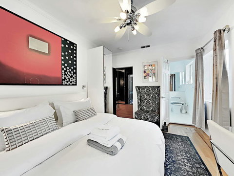 An elegantly designer bedroom boasting a luxurious KING-size beds (or 2 twin beds upon request), private balcony overlooking pool area, a sleek professional workspace, and mirrored closets that create a bright, open, and sophisticated atmosphere.