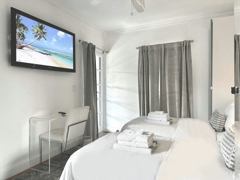An elegantly designer bedroom boasting a luxurious KING-size beds (or 2 twin beds upon request), private balcony overlooking pool area, a sleek professional workspace, and mirrored closets that create a bright, open, and sophisticated atmosphere.