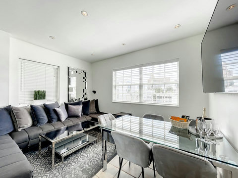 Experience comfort and entertainment in the inviting living room, boasting a U-shaped corner sofa, dining table, and a 75-inch Smart TV. 