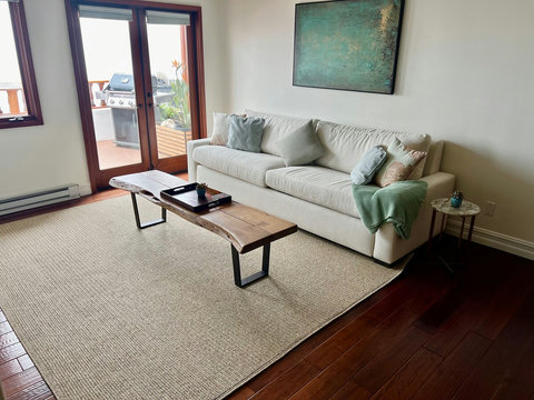 - Relax in this living room with a cloud-soft sofa, natural textures, & calming tones
- Sliding doors open to the outdoor grill area, perfect for seamless indoor outdoor living
- Earthy wood floors, coffee table, & modern art complete the tranquil vi