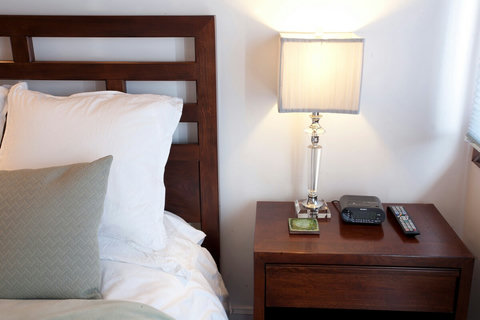 - Wake up rested with plush pillows & crisp white linens against a rich wood headboard
- Bedside lamp adds a warm evening glow, perfect for winding down with a book or show
- Includes essentials like a clock radio, remote, & a sleek modern nightstand