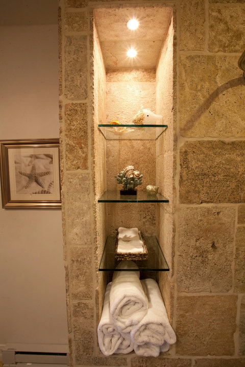 - Built in shelving with accent lighting adds character and charm to the bath space
- Stocked with rolled towels, decorative seashells, and spa like essentials for your comfort
- Earthy stone backdrop offers a cozy, coastal feel throughout
