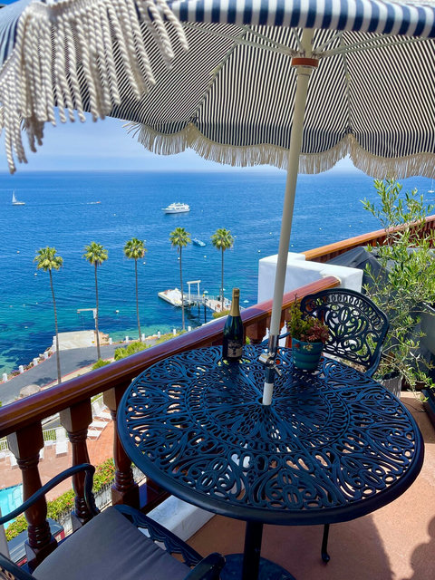 - Savor a glass of wine or a lazy breakfast with front row views of turquoise Catalina waters
- Chic wrought iron table shaded by a vintage striped umbrella sets the scene
- Palm trees sway, sailboats drift, this is pure postcard living