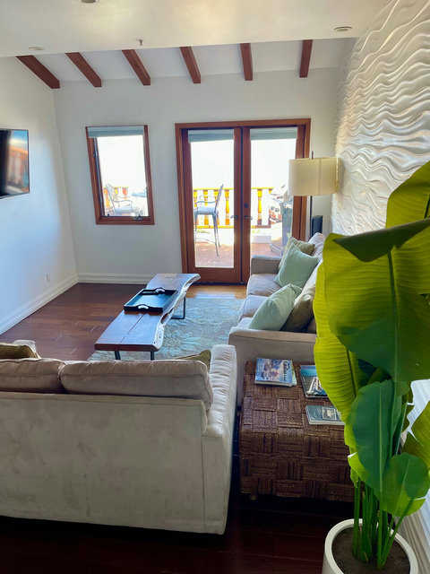 - Sun drenched living room with plush seating, earthy tones, and ocean air at your door
- Vaulted wood beams and a statement wave wall add style and depth
- Steps into your private balcony, ideal for morning coffee or golden sunsets