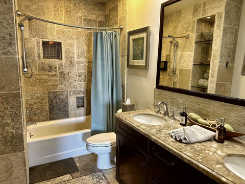 - Elegant bathroom with natural stone walls and a curved shower rod for added space
- Double sink vanity with marble countertops and large mirror for a stylish touch
- Coordinated décor and spa amenities enhance comfort and style
