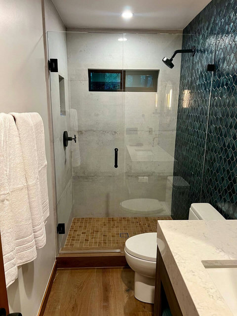 - Refresh in the glass enclosed rainfall shower with elegant emerald toned tile accents
- Warm wood & clean lines offer a serene, modern contrast to the natural stone floor
- Plush towels, designer lighting & quartz countertops elevate the spa like f