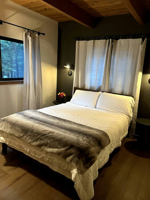 - Rest easy in a peaceful bedroom retreat with crisp white bedding and soft lighting
- Wake to serene forest views through double windows dressed in flowing curtains
- Exposed beams, wood floors, and modern accents create a cozy yet chic vibe