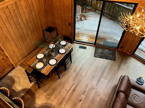 - Gather around the rustic wooden dining table set under soft chandelier light
- Floor to ceiling glass doors open to a serene deck, blending indoor and outdoor charm
- Enjoy your meals with natural light, scenic views, and warm timber surroundings