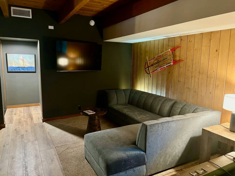 - Relax in the oversized velvet sectional & catch a movie on the mounted flat screen TV
- Retro decor like the vintage sled & rustic wall paneling create a nostalgic vibe
- Cozy carpeted space perfect for movie nights or laid back afternoon lounging