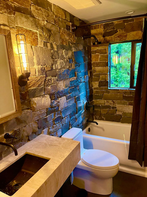 - Spa like relaxation surrounded by hand laid natural stone walls
- Enjoy a hot soak in the deep tub, framed by a picture window looking out to greenery
- Industrial lighting, matte black fixtures, and stone textures create a luxe rustic vibe