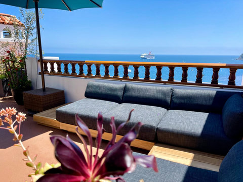 - Relax on the plush outdoor sectional under a large umbrella with uninterrupted sea views
- Tropical plants and a distant cruise ship add vibrant charm to this sunny deck
- Perfect for unwinding with cocktails or catching golden sunsets