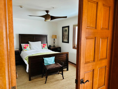 - Step into a cozy guest room with bold wood furnishings & floral pillows for a vibrant touch
- Ceiling fan & large windows provide airflow & natural light for restful nights
- Soft rug & decorative bench complete this inviting and stylish retreat

